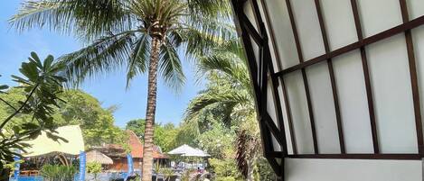 A covered outdoor seating area with a table and chairs, overlooking a water body and palm trees.
