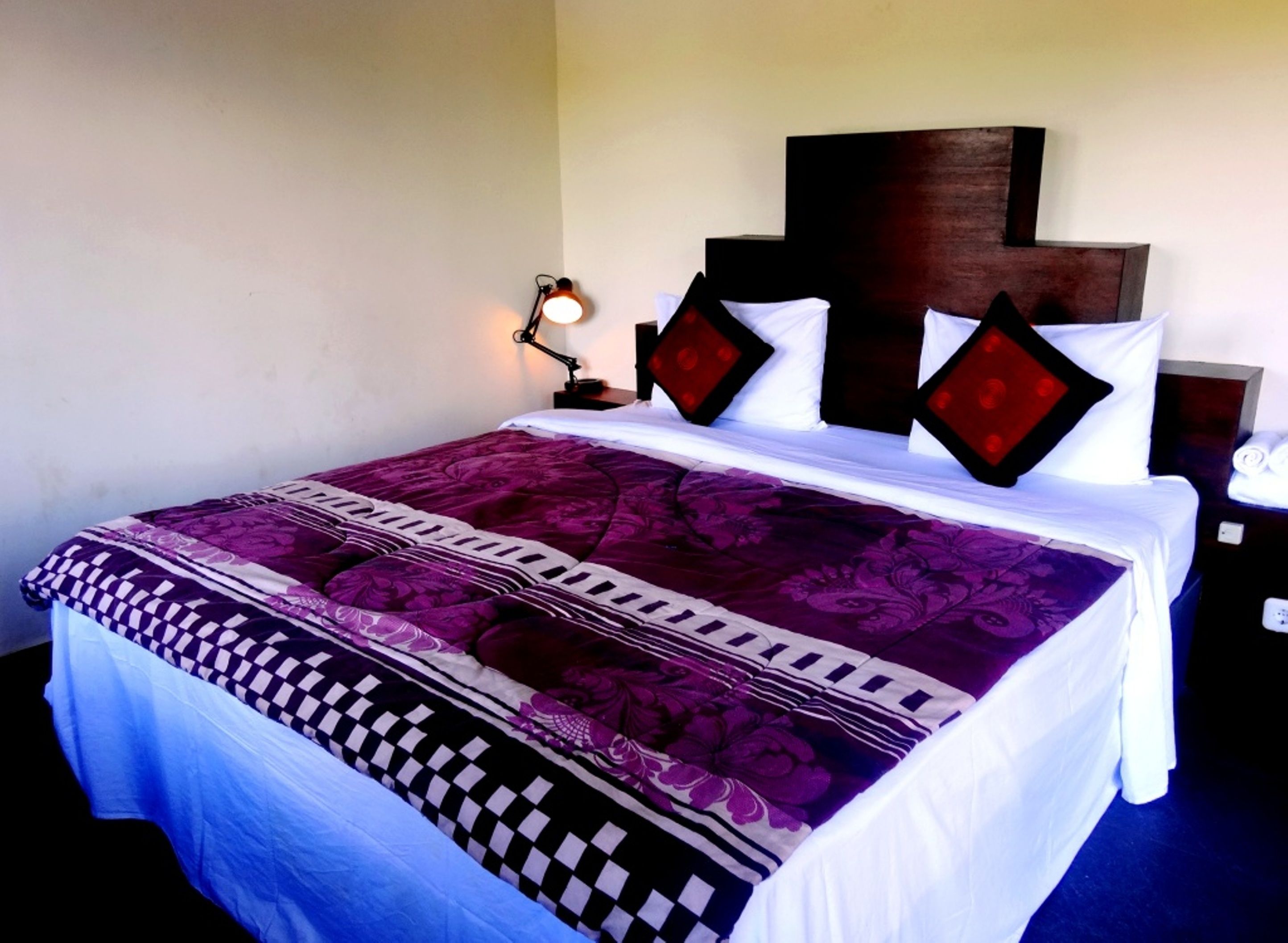 A neatly made bed with a patterned bedspread, a wooden headboard, and a bedside lamp.