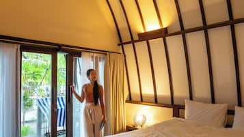 Un dormitorio con cama, mesita de noche, lámpara y vistas al exterior a través de una puerta corredera.