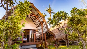 Un bungalow doté d’un toit de chaume, entouré d’une végétation luxuriante et de palmiers.