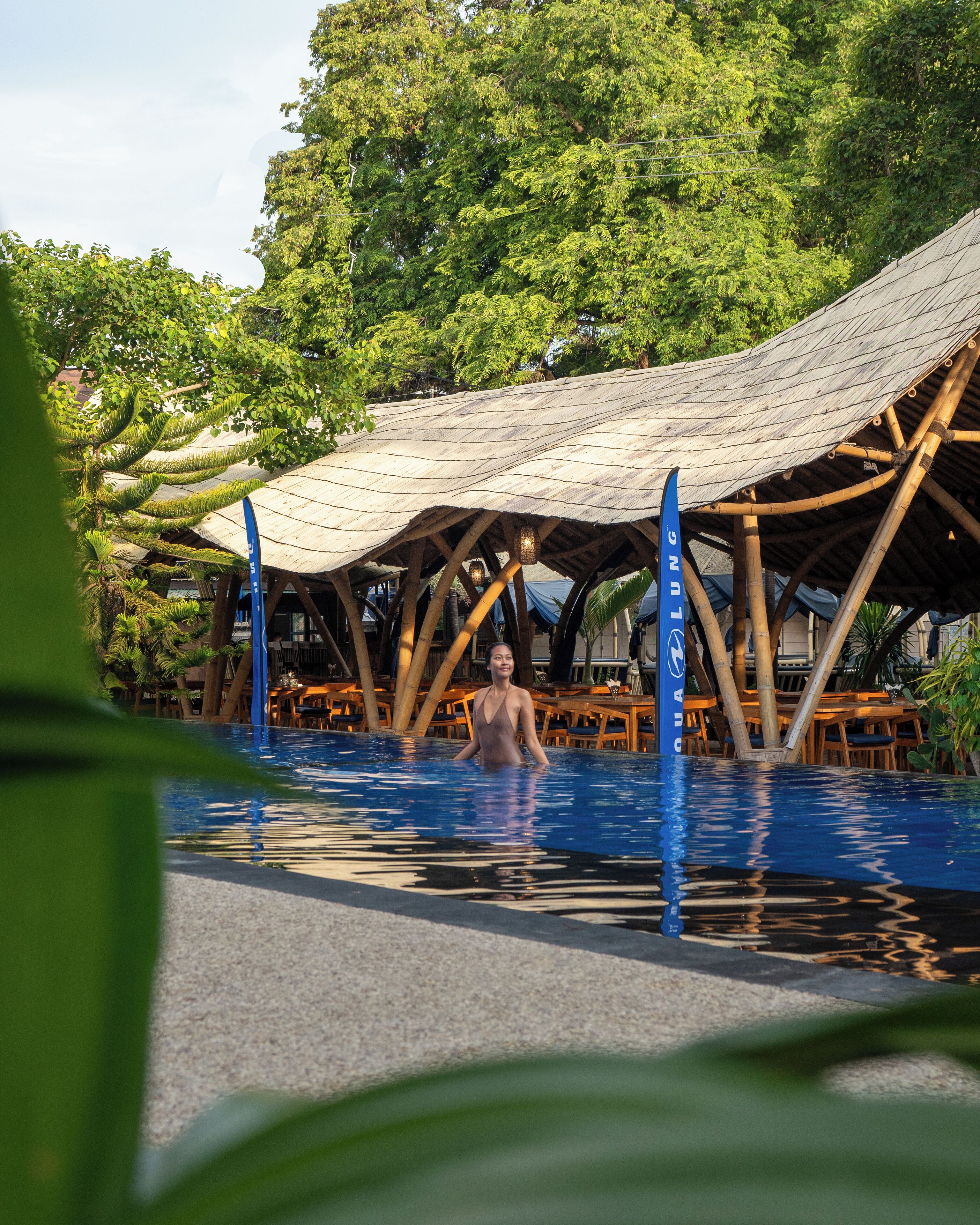 A pool area with a wooden structure overhead, surrounded by lush greenery.