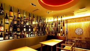 A bar area with multiple tables and chairs, shelves with bottles, and a decorative wall with hanging elements. - Central Hotel Okayama (Okayama)