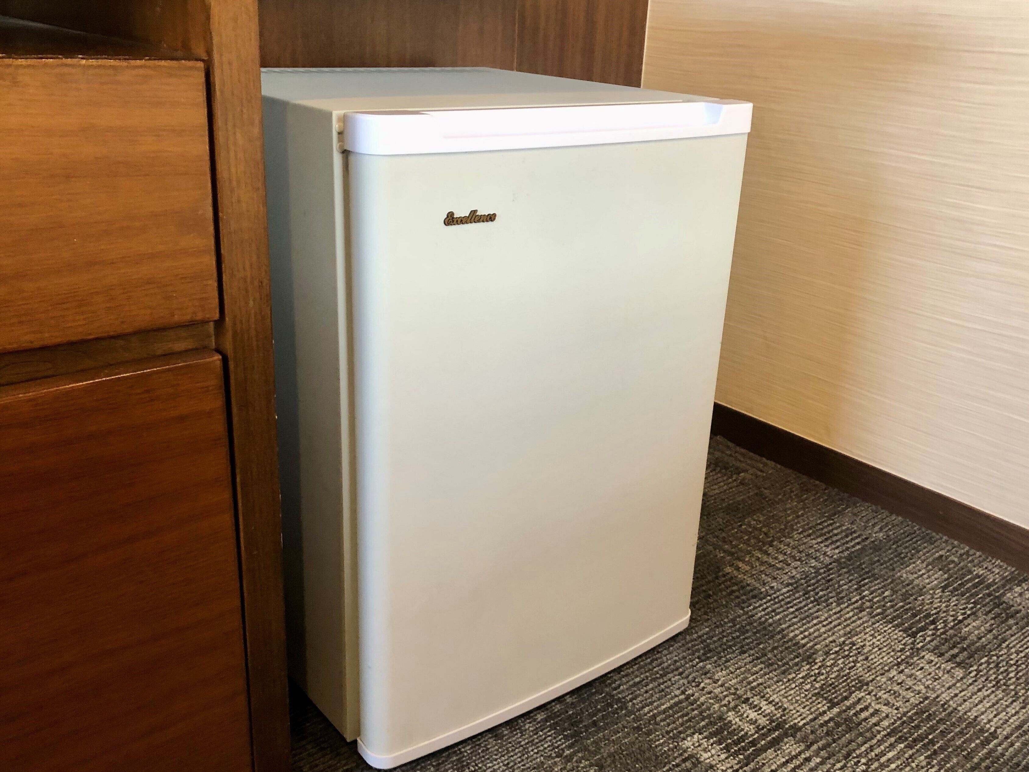 A white refrigerator in a corner of a room with wooden cabinetry and a carpeted floor.