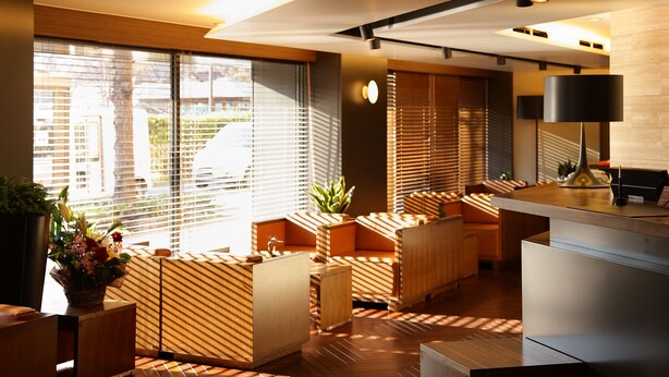 A modern hotel lobby with a wooden reception desk, seating area, and large windows with blinds. - Central Hotel Okayama (Okayama)