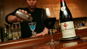 A person pouring a drink into a glass at a bar with a bottle of wine labeled "Chambertin" and a blue cocktail glass. - Central Hotel Okayama (Okayama)