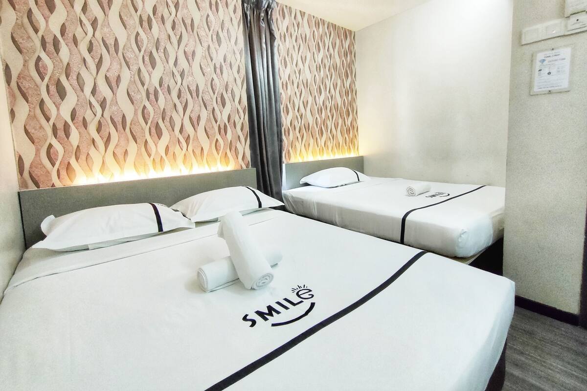 A hotel room with two beds, each with a pillow and a rolled towel. The beds have a logo on the bedspread.