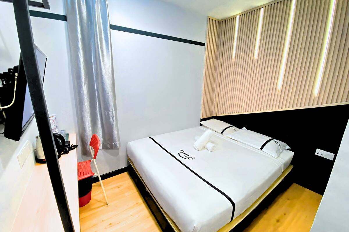 A modern hotel room with a bed, a wooden floor, a curtain, and a wall-mounted light fixture.