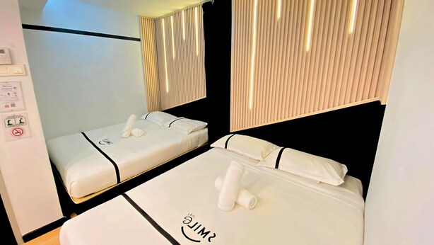 A hotel room with two beds, each with white linens and a smiley face design. There is a ceiling fan, a wall-mounted control panel, and a window with vertical blinds. - Seeds Hotel Setiawangsa (Ampang)