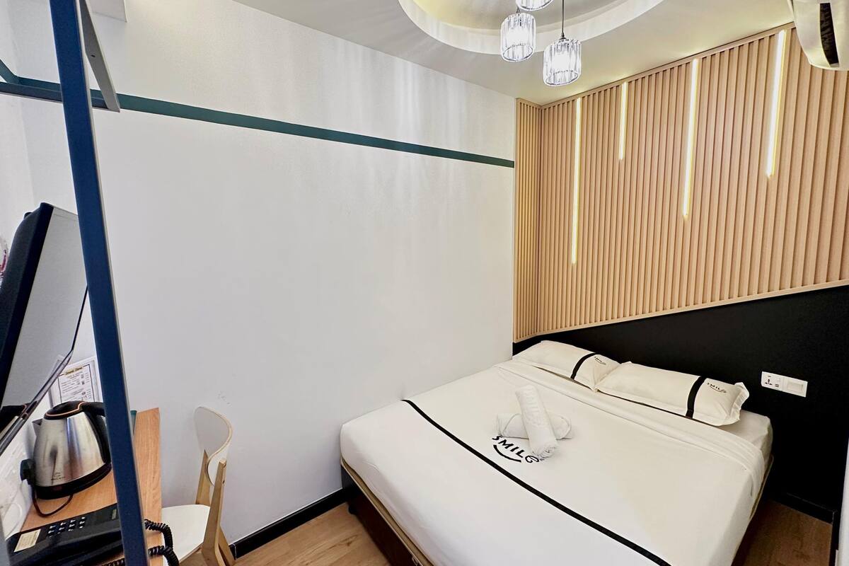 A hotel room with a bed, a desk with a telephone, a chair, and a ceiling light fixture.