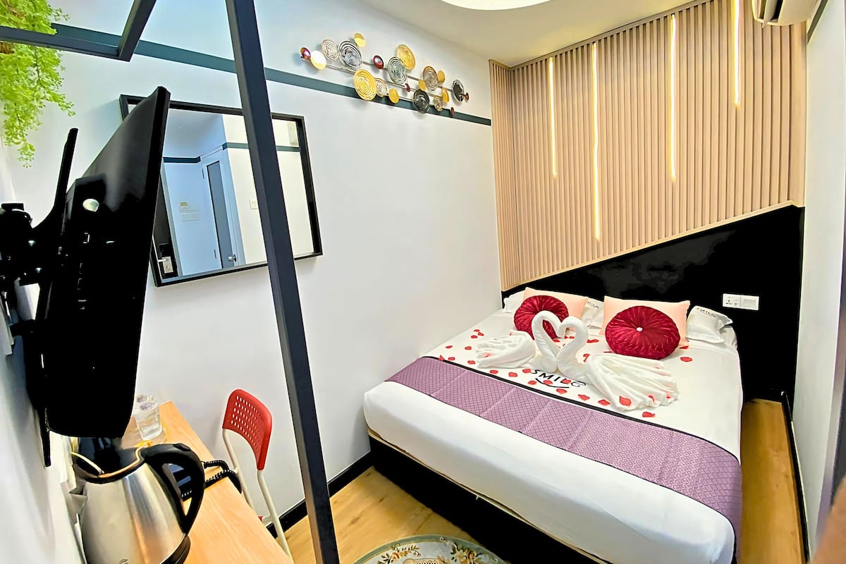 A hotel room with a bed, a desk, a chair, a TV, and a wall-mounted air conditioner.