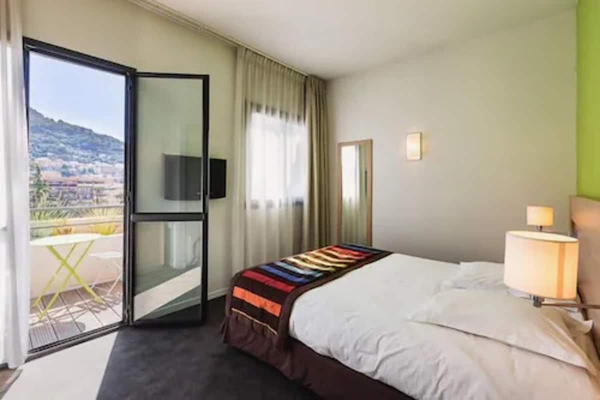 Una habitación de hotel con cama, televisión, balcón y vistas, además de una lámpara.