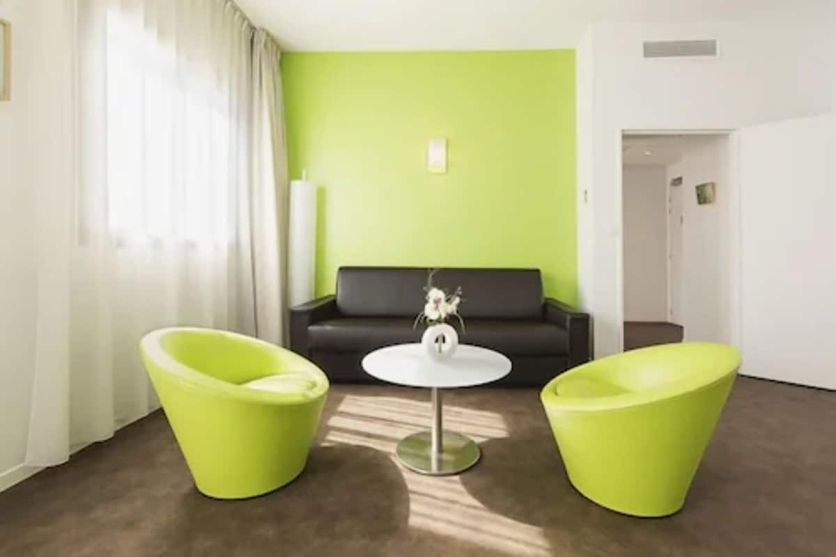 Una habitación moderna con una pared de acento verde, un sofá negro y dos sillas verdes alrededor de una pequeña mesa blanca.
