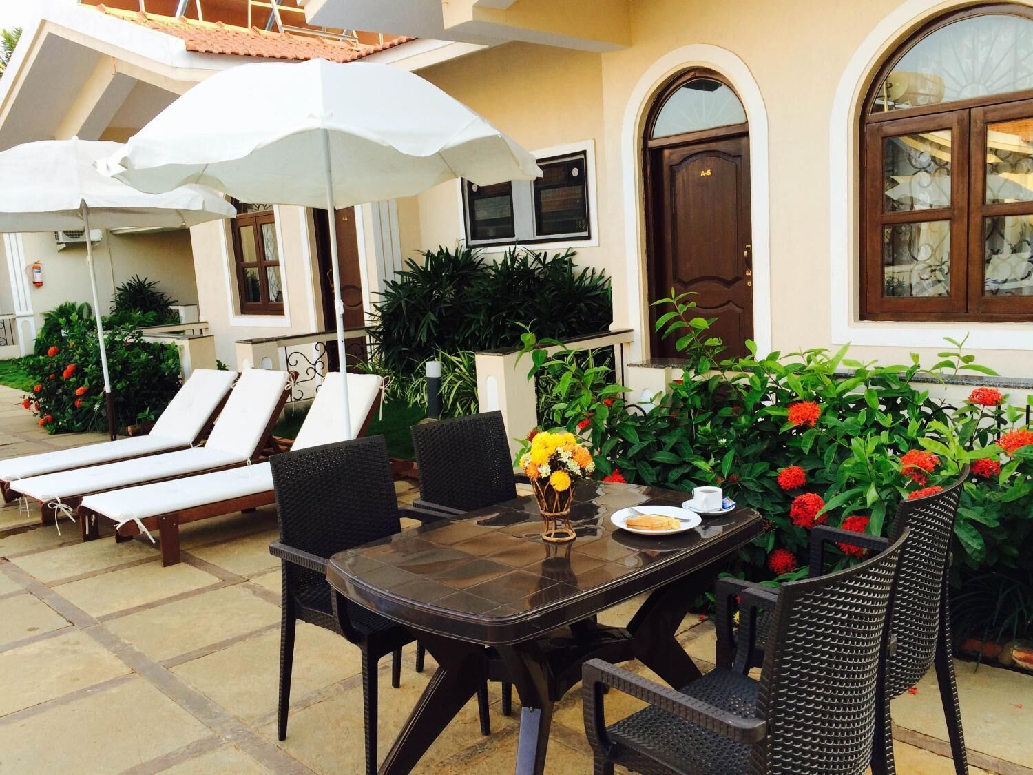 Un patio con sillones de descanso, una mesa con un florero y plantas en macetas.