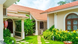 A house with a tiled roof, a garden with a stone pathway, and a variety of plants. - Jacks Resort (Vagator)