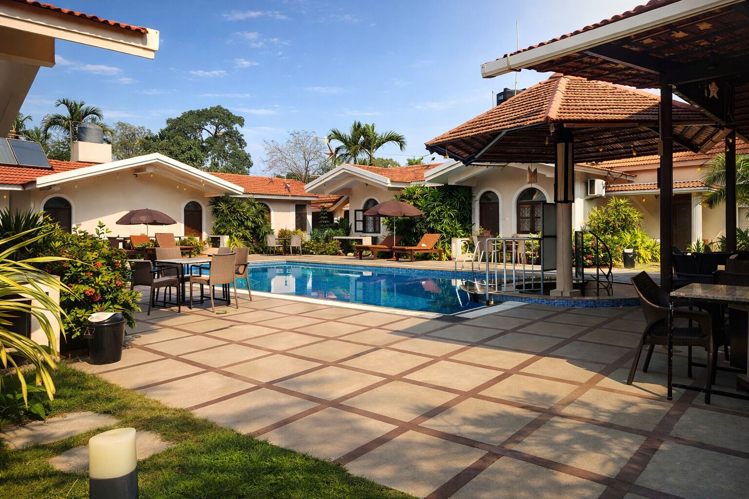 Un área de piscina con suelo de baldosas, sillas de descanso y sombrillas.