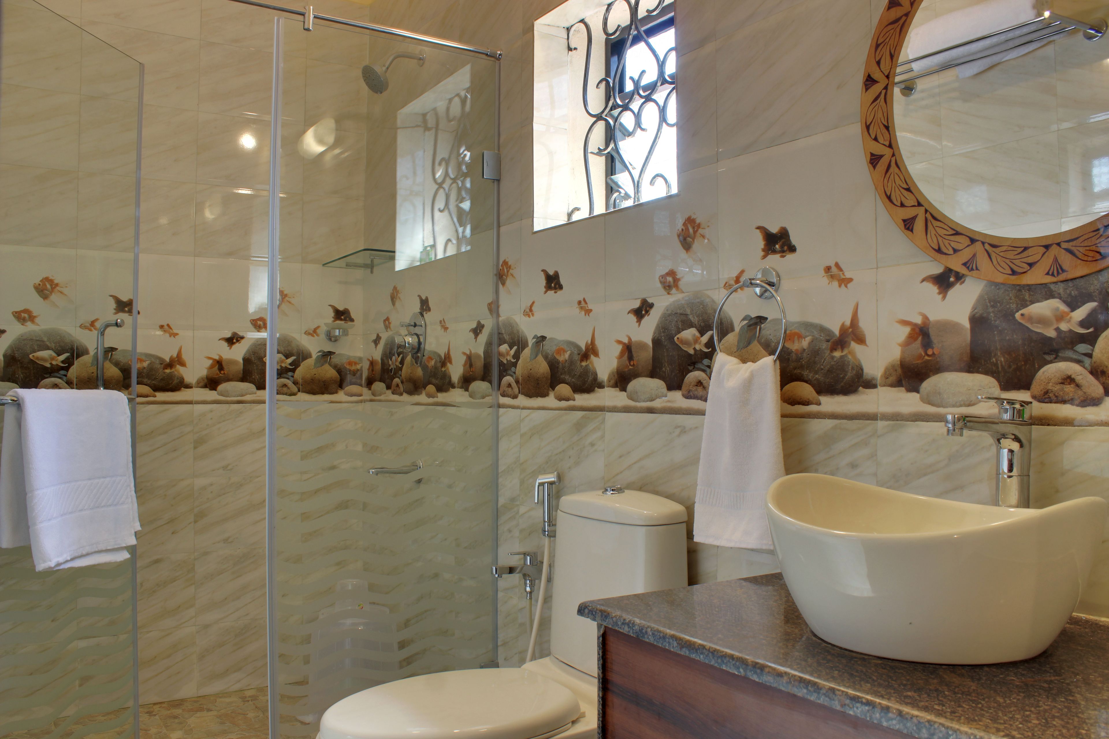 A bathroom with a glass shower enclosure, a sink with a decorative basin, and a wall with a fish mural.