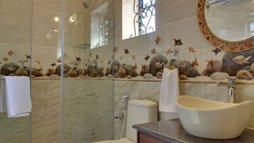 A bathroom with a glass shower enclosure, a sink with a decorative basin, and a wall with a fish mural.