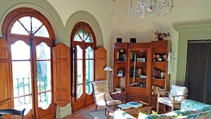 A cozy living room with wooden furniture, a bookshelf, and large windows. - Villa Colle Olivi (Pescia)