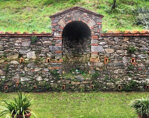 A stone wall with a tunnel entrance, surrounded by greenery. - Villa Colle Olivi (Pescia)