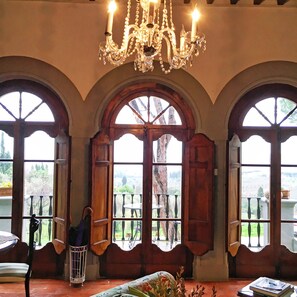 A room with a chandelier, arched windows, and a view of the outdoors. - Villa Colle Olivi (Pescia)