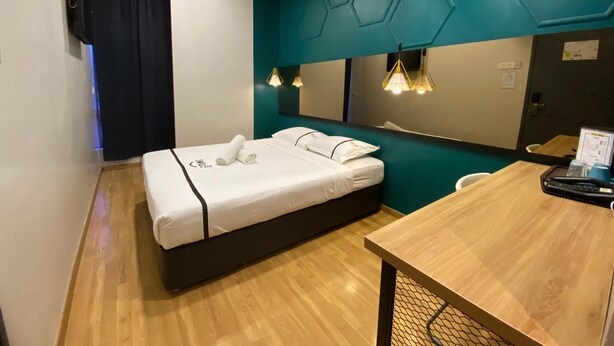 Een moderne hotelkamer met een bed, een houten bureau, een spiegel en een wand in teal.
