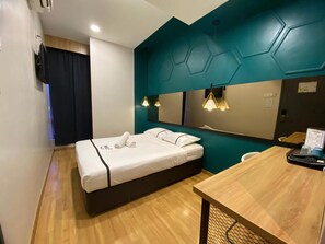 Una camera d'albergo moderna con un letto, una scrivania in legno, uno specchio e una parete verde acqua.