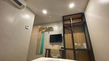A hotel room with a bed, a desk, a chair, a TV, and a wardrobe.