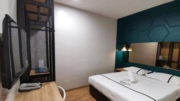 Une chambre d’hôtel équipée d’un lit, d’un bureau, d’une chaise, d’un miroir et d’un téléviseur fixé au mur.