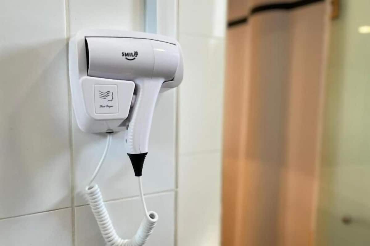 Un sèche-cheveux fixé au mur, doté d’un cordon, d’une prise de courant et d’un panneau de commande avec un symbole représentant une main.