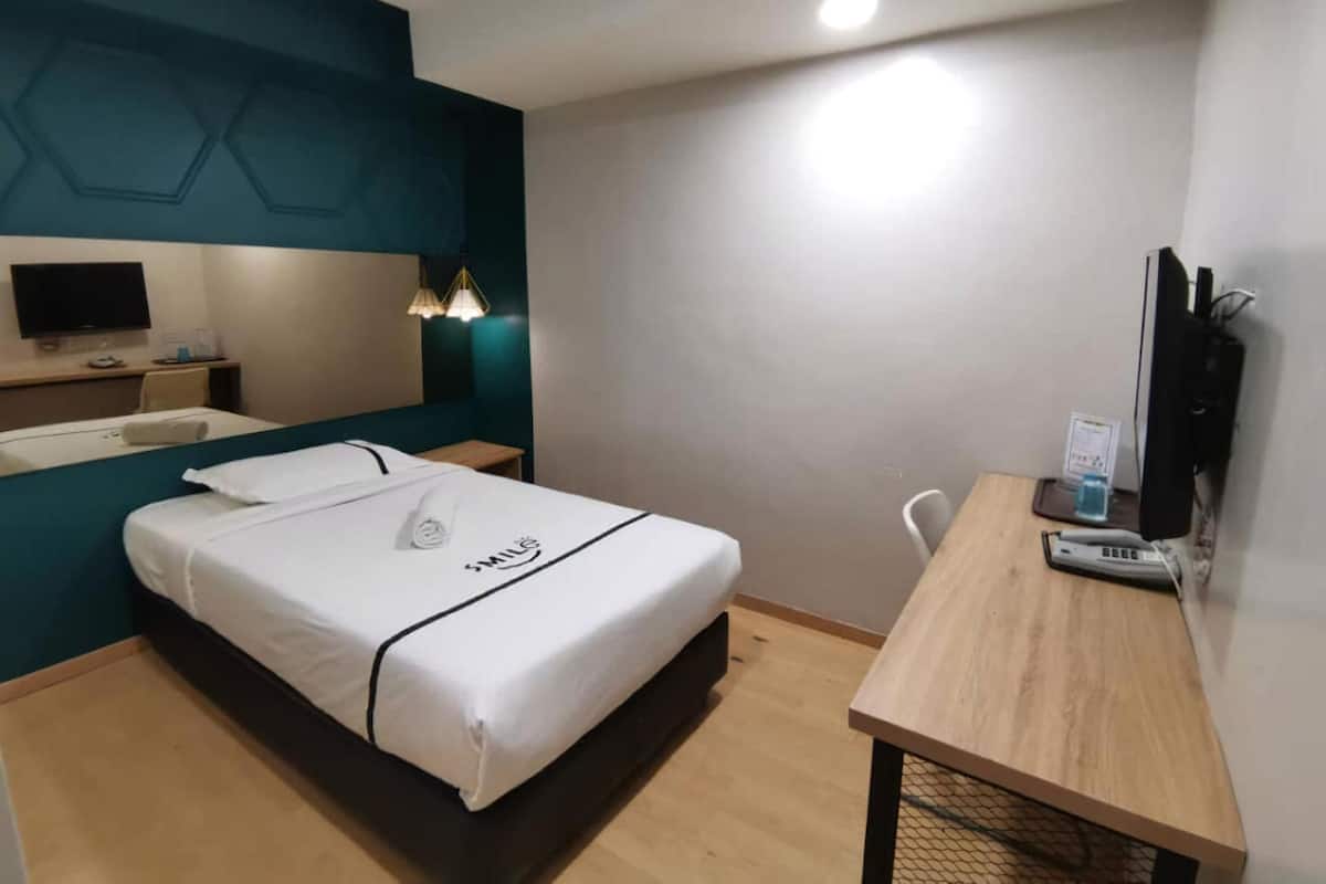 Une chambre d’hôtel avec un lit, un bureau, une chaise, une télévision et une lampe.