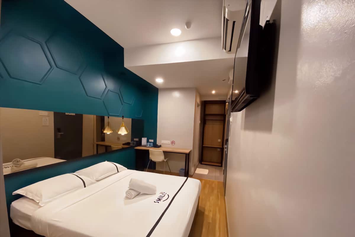 Une chambre d’hôtel avec un lit, un bureau, une chaise et un miroir.