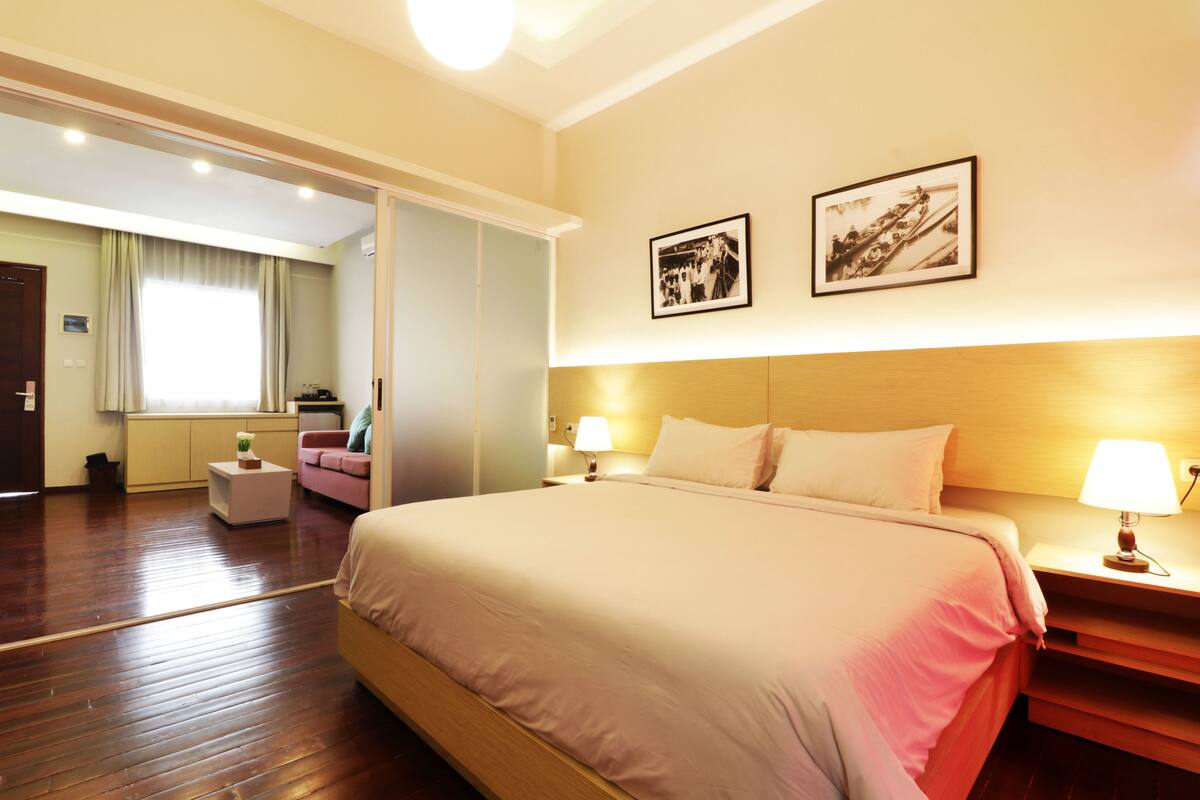 Habitación de hotel con una cama grande, lámparas de noche, un cabecero de madera y dos cuadros en la pared.