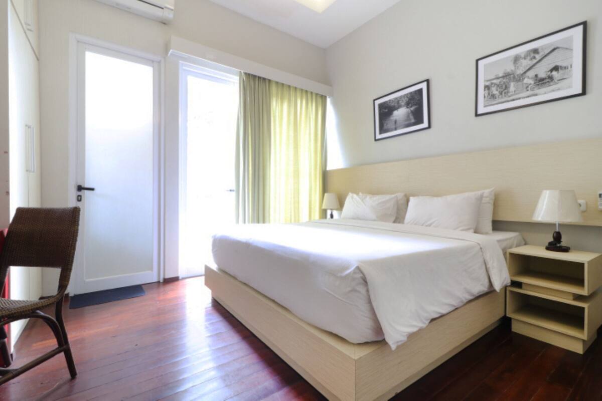 Habitación de hotel con una cama grande, una silla, una mesita de noche y dos cuadros en la pared.