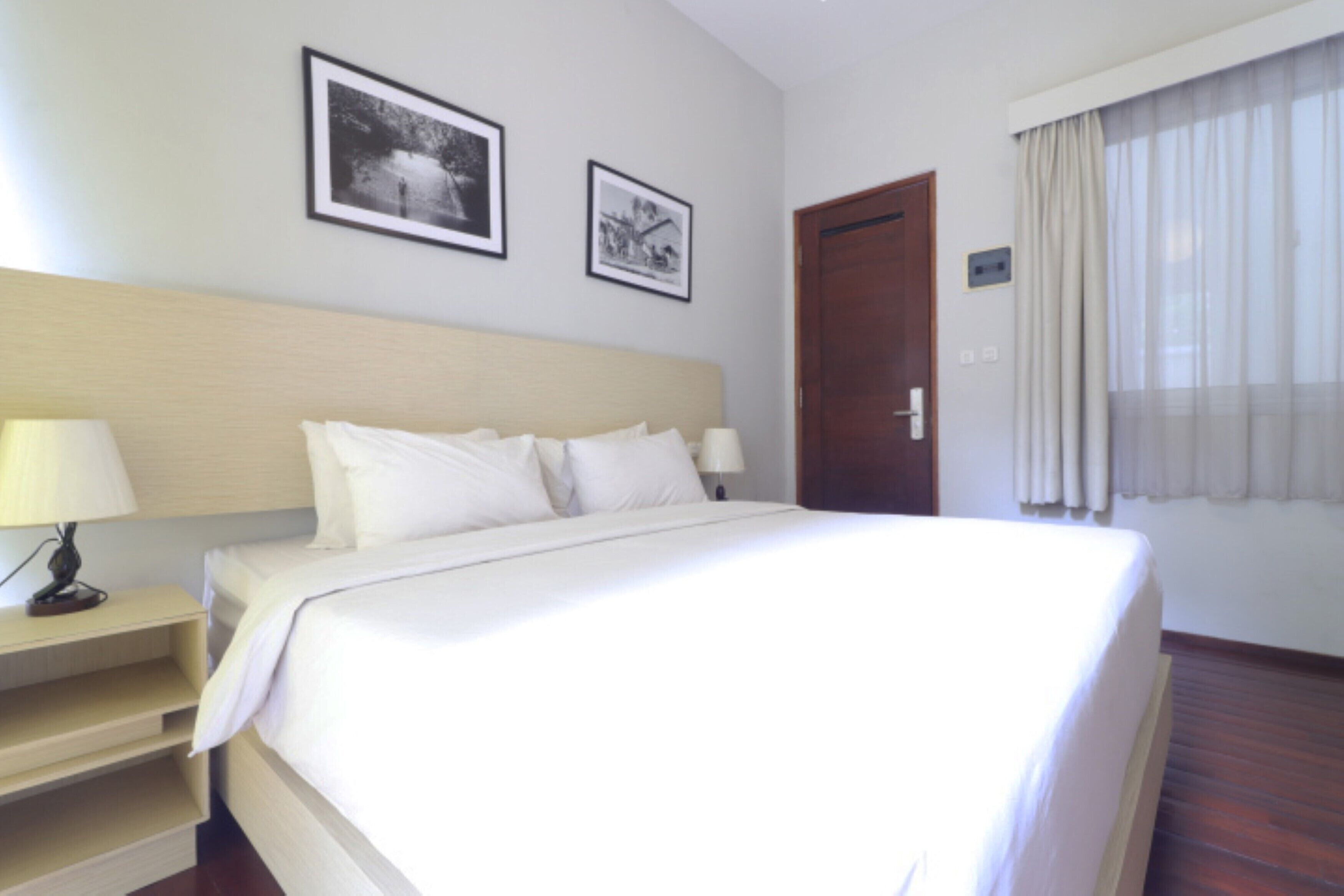 A hotel room with a large bed, two bedside tables with lamps, a wooden headboard, and two framed pictures on the wall.