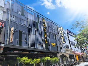 En moderne hotelbygning med et tydeligt 'HOTEL' skilt, en synlig indgang og en parkeringsplads med motorcykler.