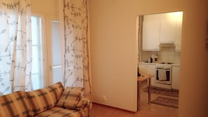 A living room with a plaid sofa and a small table, leading to a kitchen with white cabinets and a stove. - City Apartment Lappeenranta (Lappeenranta)