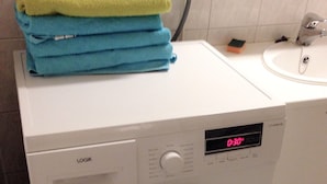 A front-loading washing machine with a digital display, a stacked towel rack, and a small sink with a faucet. - City Apartment Lappeenranta (Lappeenranta)