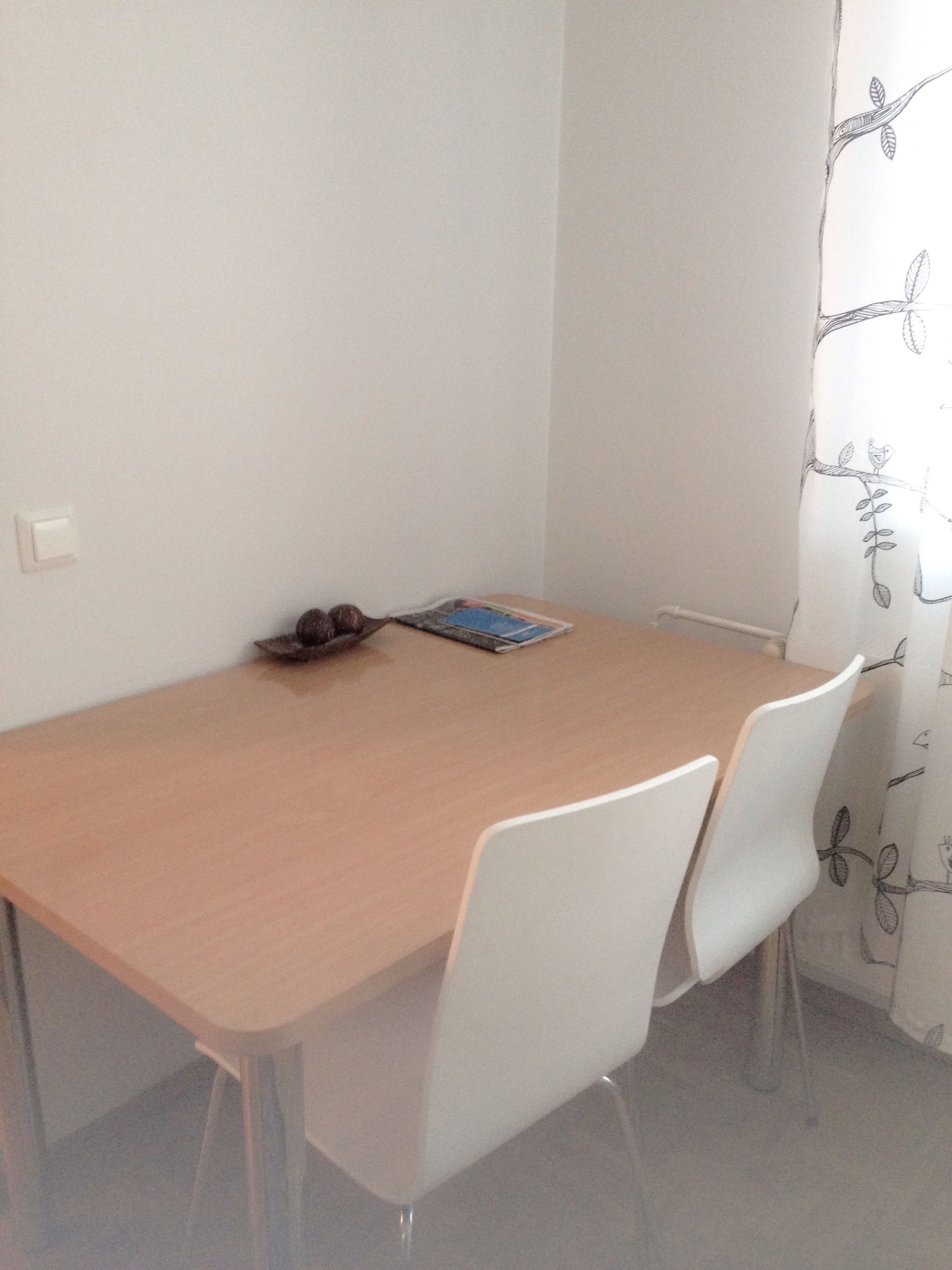A dining table with four white chairs, a magazine, and a small decorative item on the table.