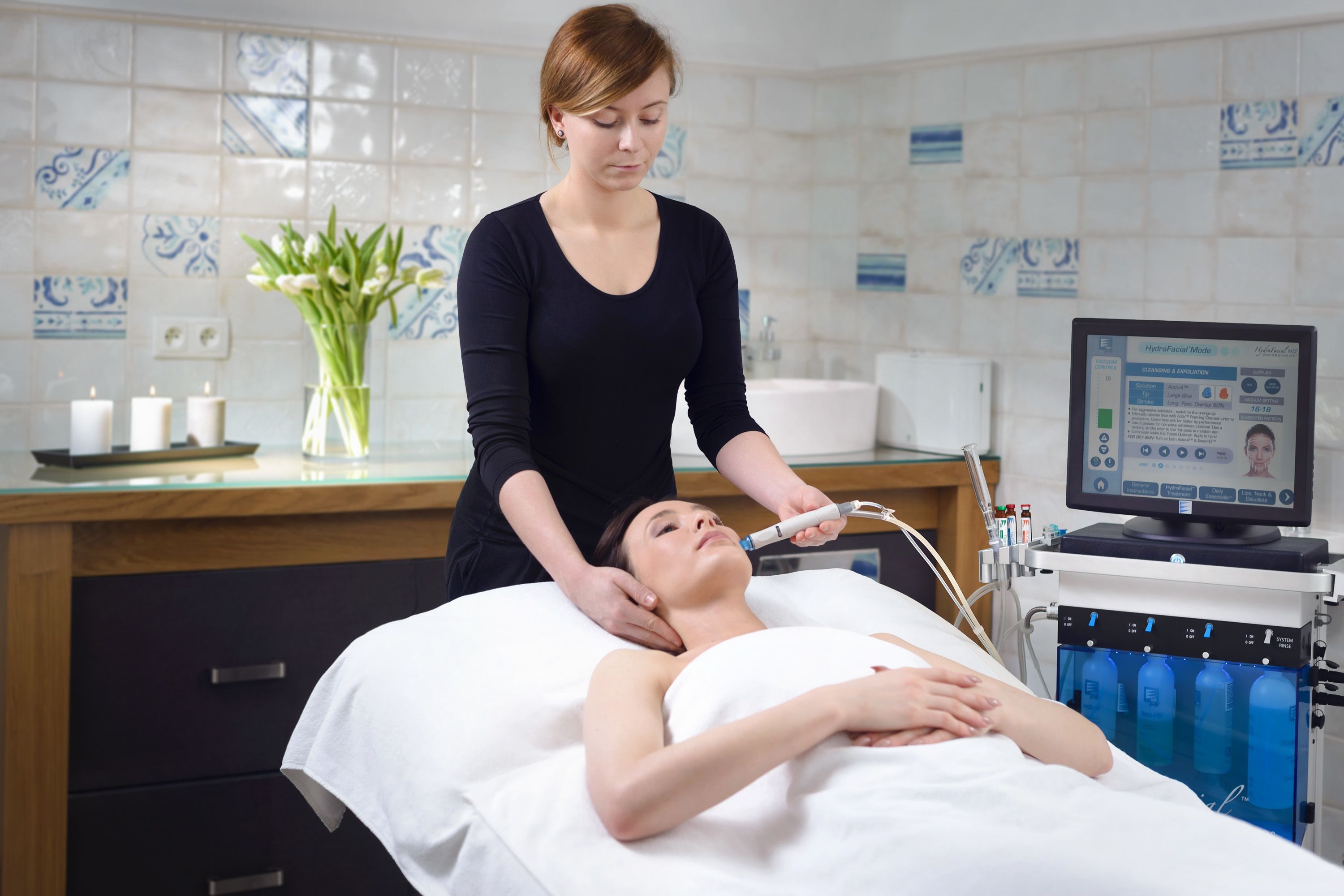 A medical treatment room with a patient lying on a bed, a practitioner using a device on the patient, and a computer monitor displaying a treatment plan.