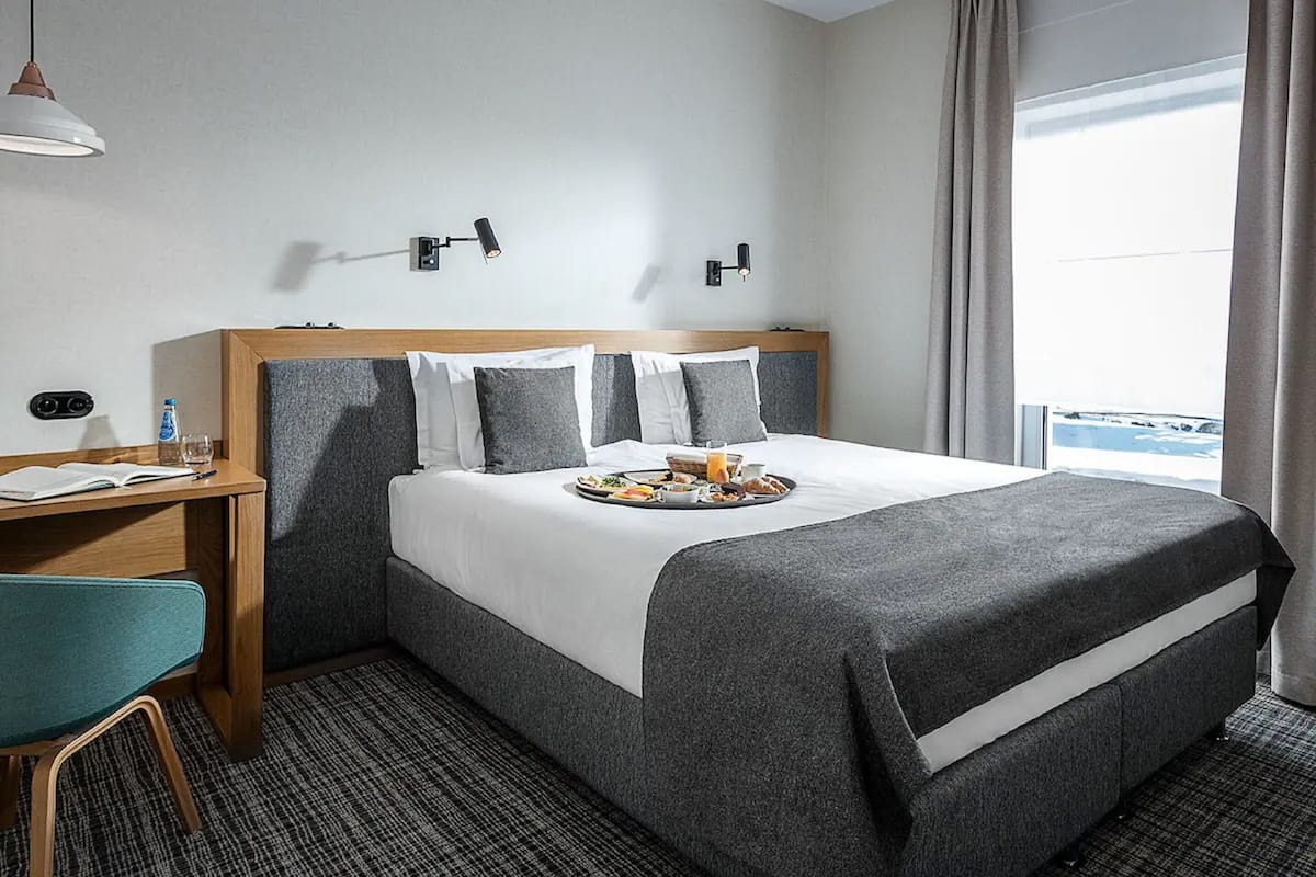 Une chambre d’hôtel avec un lit, un bureau, une chaise et une fenêtre avec des rideaux.