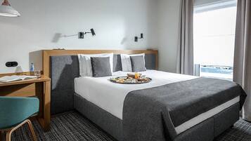 A hotel room with a bed, a desk, a chair, and a window with curtains.