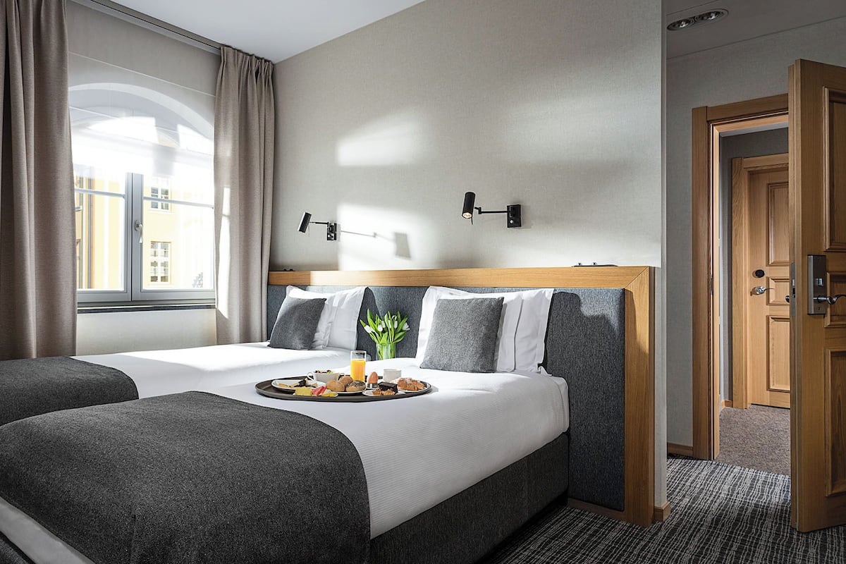 Une chambre d’hôtel avec deux lits, un plateau de petit-déjeuner, une fenêtre avec des rideaux, une lampe fixée au mur et une porte.