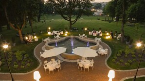 An outdoor patio area with round tables and chairs, surrounded by potted plants and a central fountain.