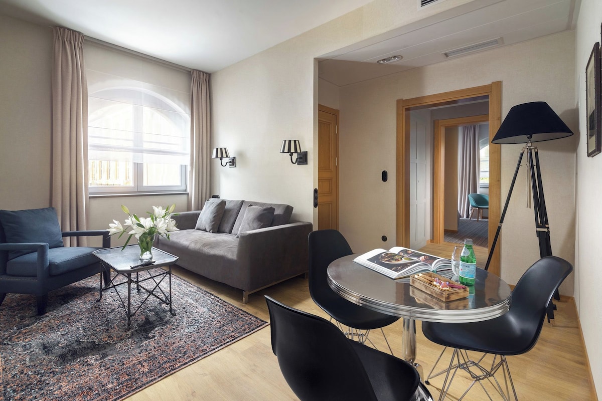 A modern living room with a grey sofa, a coffee table, and a dining area with a glass table and chairs.