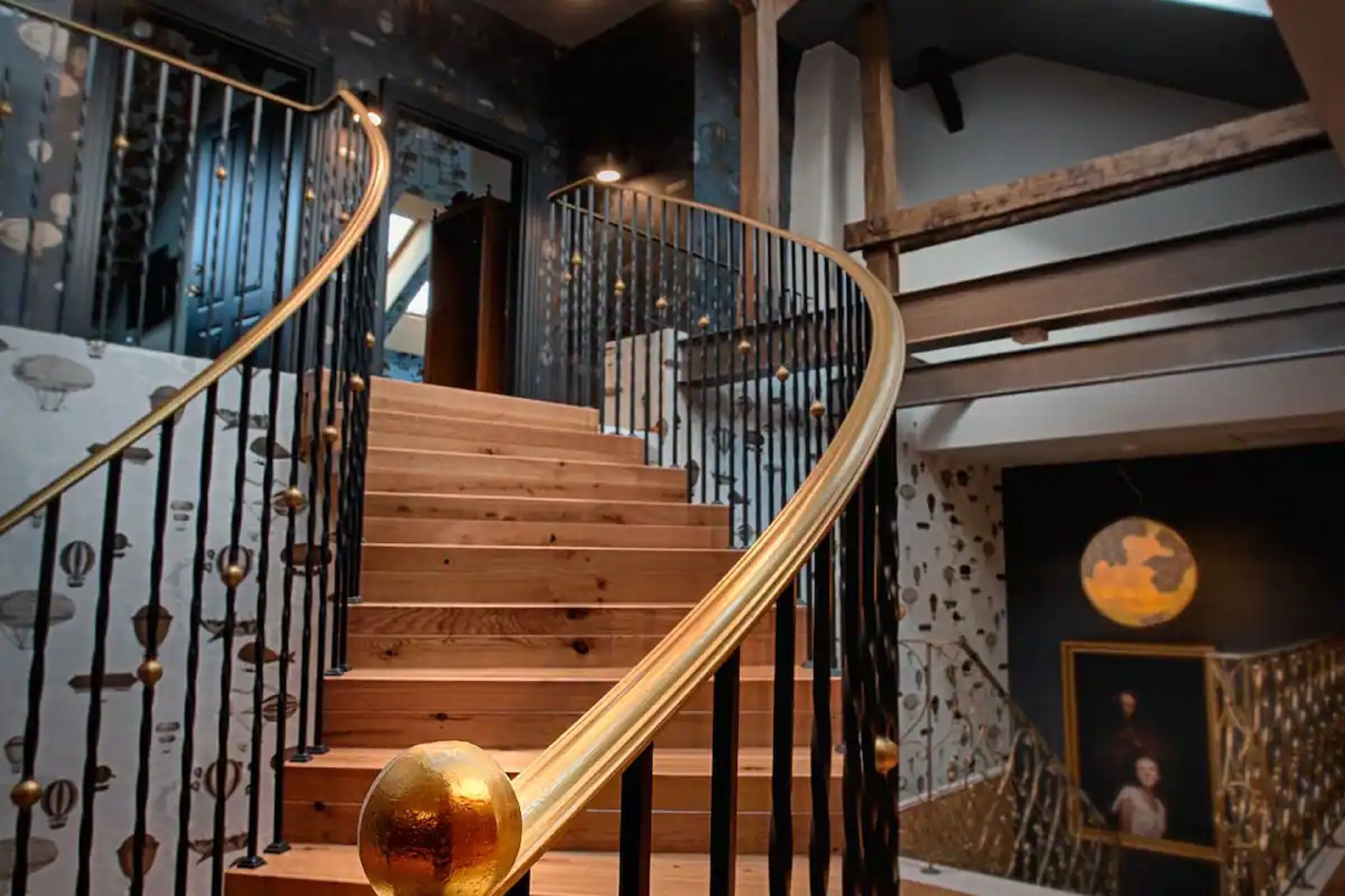 Un escalier en colimaçon avec des marches en bois et des rampes en métal noir, menant à l’étage supérieur.