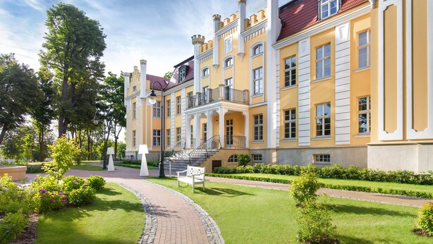 A large, yellow building with a grand entrance and a well-maintained garden.