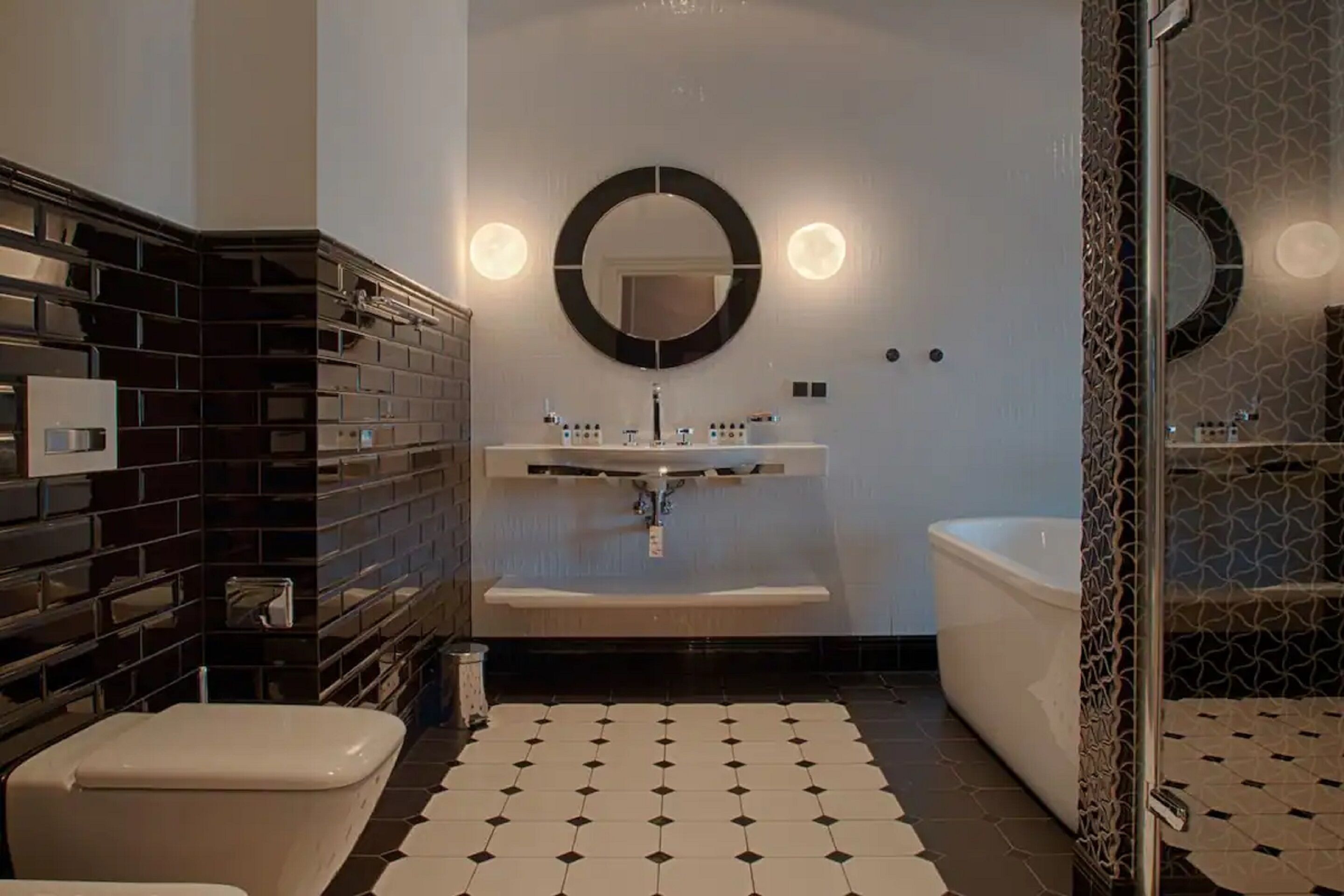 Un baño moderno con suelo de baldosas blanco y negro, un lavamanos central con espejo y una bañera.