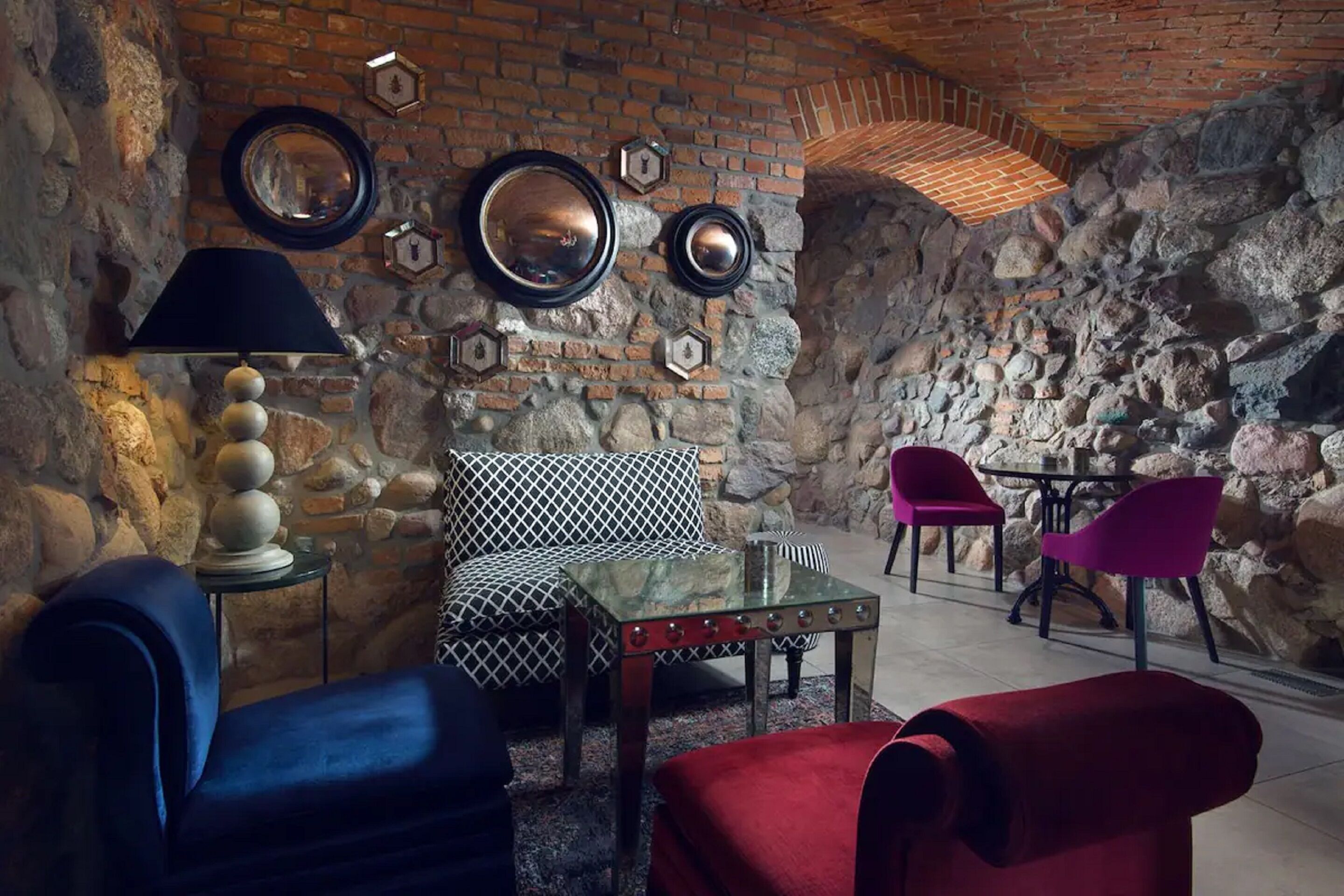 Une pièce chaleureuse avec un mur en pierre, un canapé à motifs, une table basse en verre et un fauteuil rouge.
