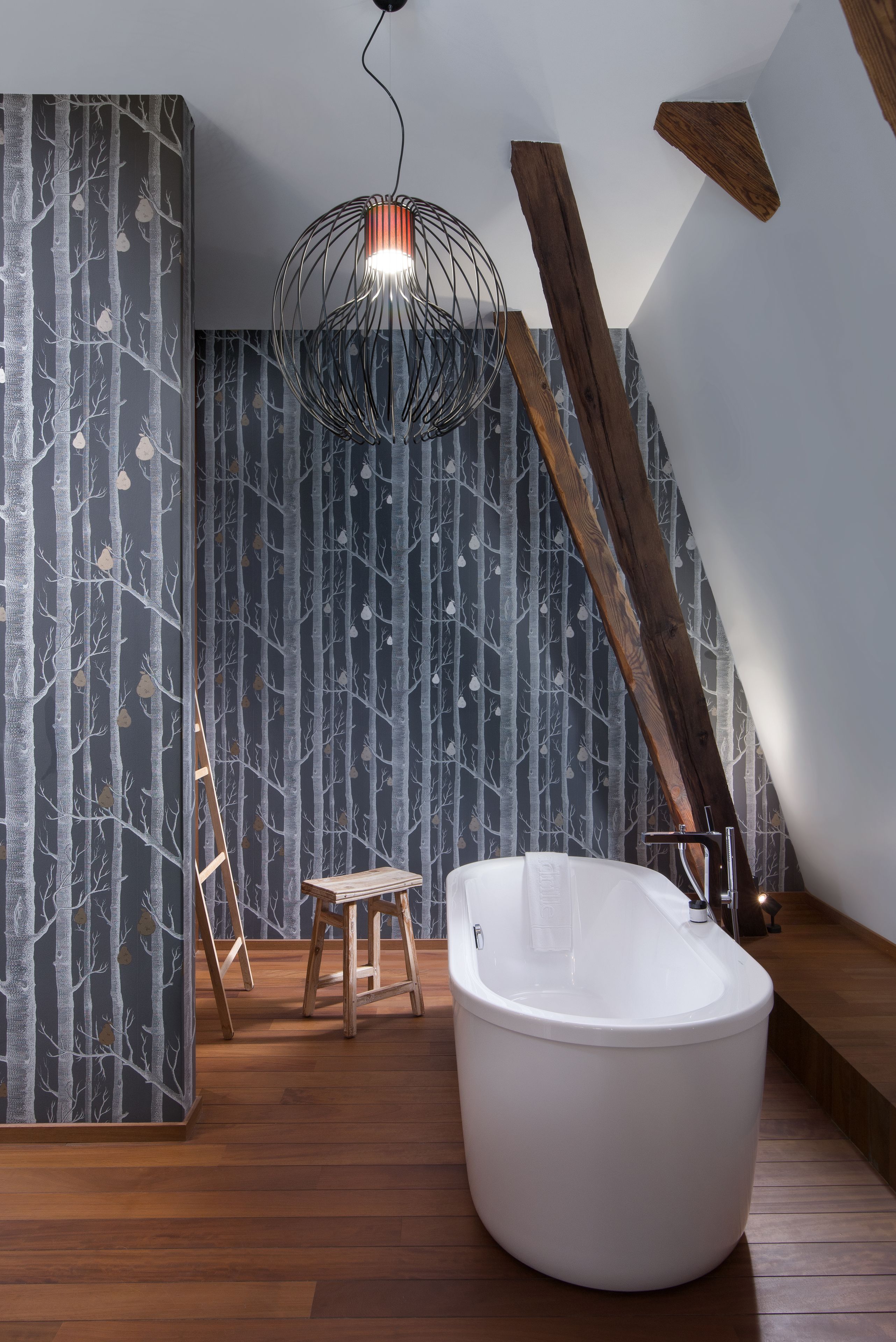 A modern bathroom with a freestanding bathtub, wooden flooring, and a sloped ceiling.