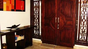 Una puerta doble de madera con detalles metálicos intrincados, una consola de madera oscura con libros y un cuadro abstracto y colorido sobre la puerta.